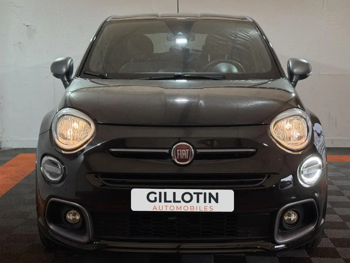 Vue frontale d'une FIAT 500X noire avec phares allumés et logo Fiat centré sur la calandre.