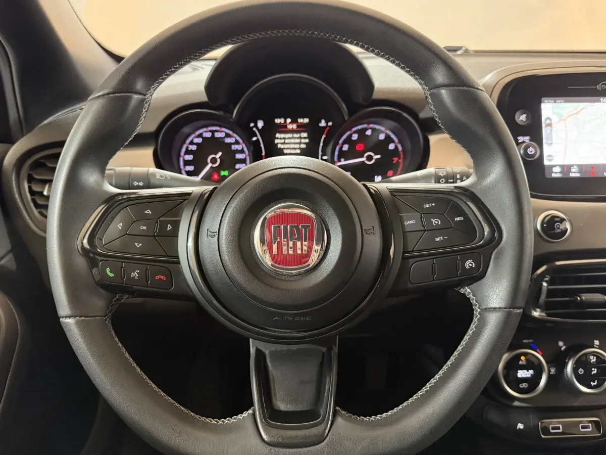 Volant cuir noir de Fiat 500X 2021 avec commandes multifonctions et tableau de bord numérique en arrière-plan.