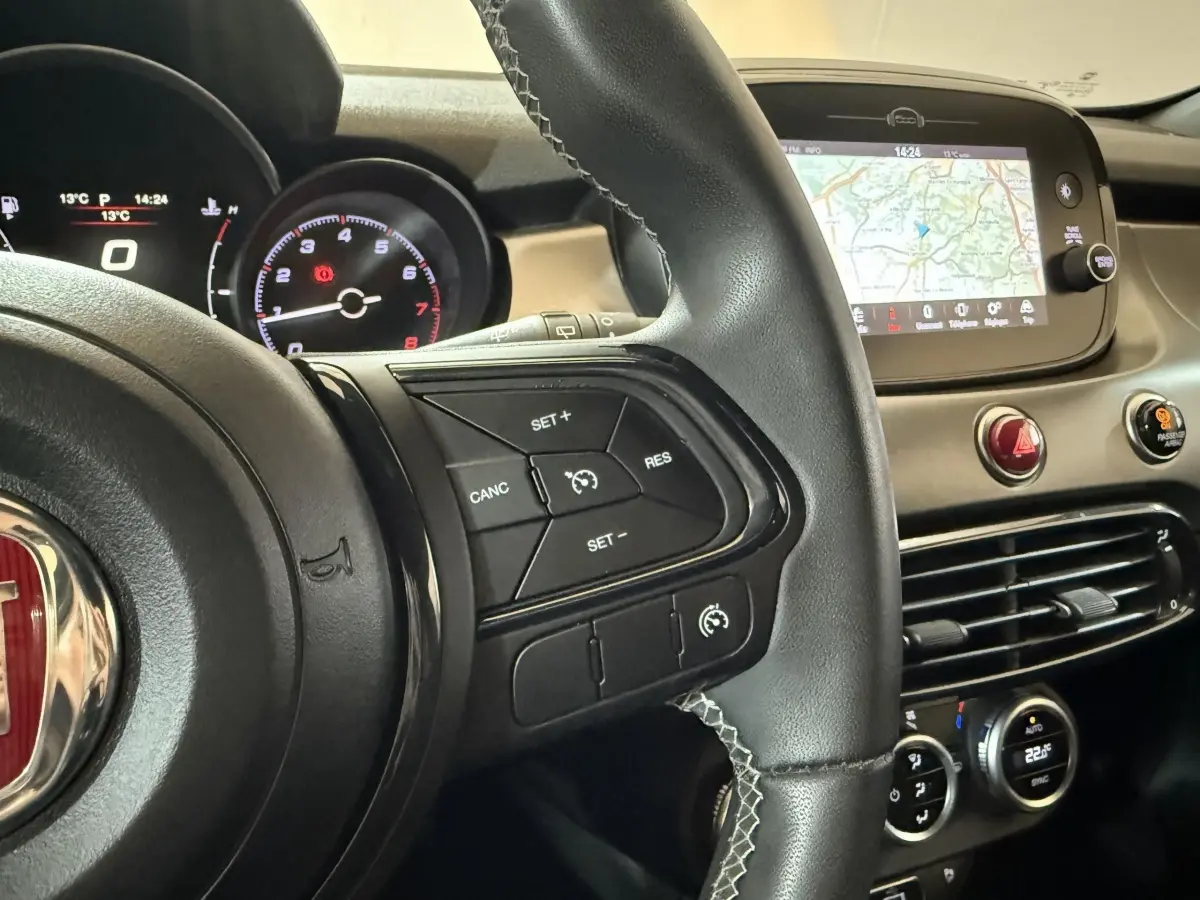 Vue rapprochée du volant cuir noir et du tableau de bord avec écran tactile et commandes du Fiat 500X noir 2021.