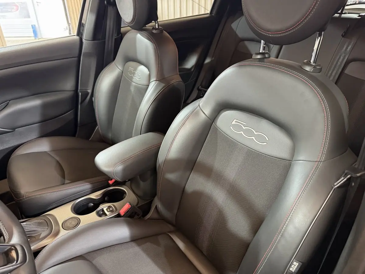 Gros plan sur les sièges avant noirs en cuir et tissu de la Fiat 500X 2021 avec logo 500 brodé et surpiqûres rouges.