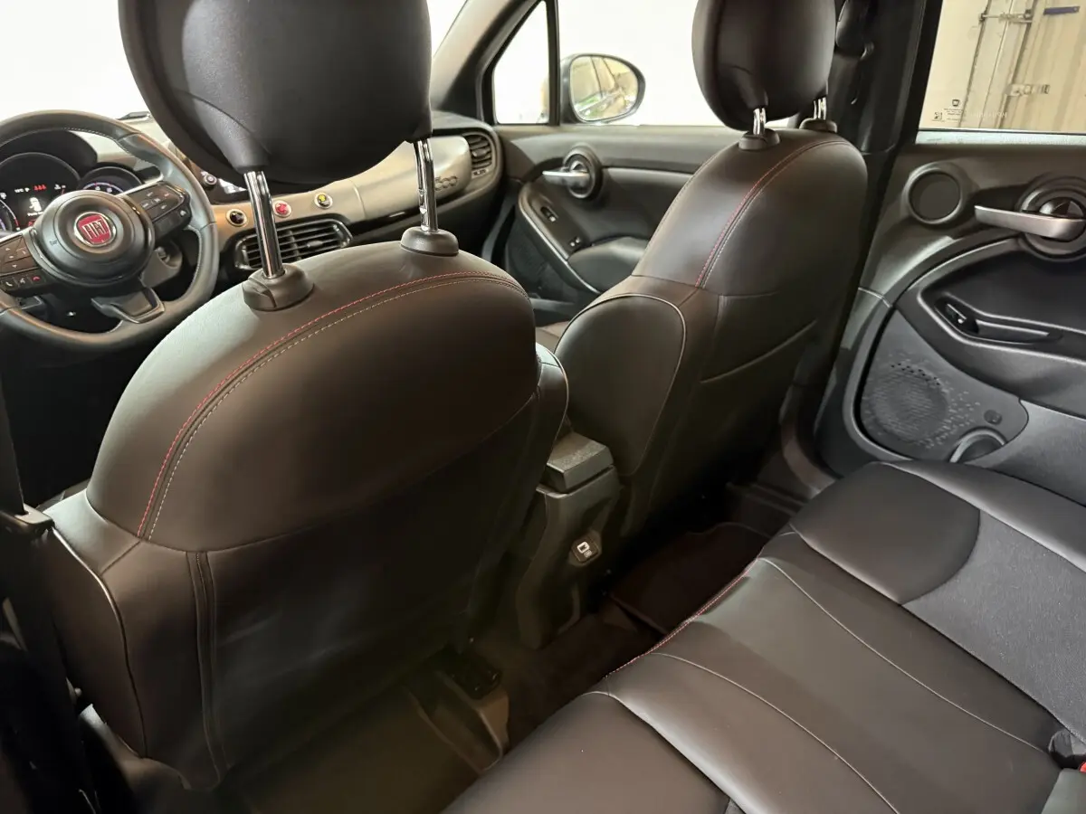 Intérieur arrière noir de la Fiat 500X 2021, vue depuis la banquette arrière vers les sièges avant en cuir avec surpiqûres rouges.