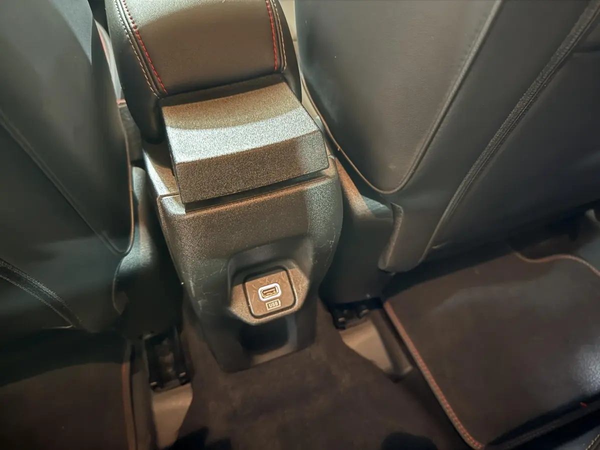 Prise USB arrière entre les sièges noirs avec surpiqûres rouges dans le Fiat 500X noir 2021.