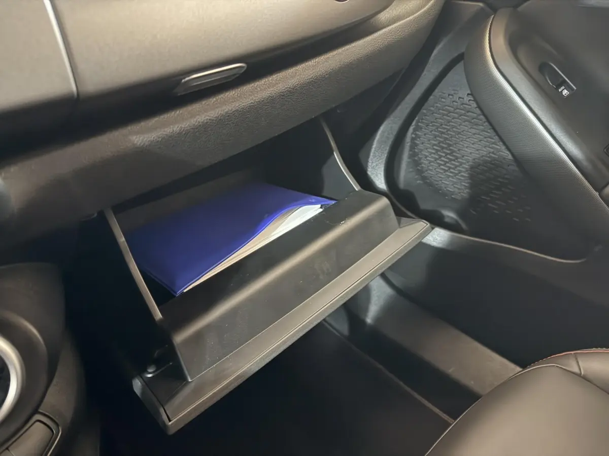 Gant de boîte à gants ouvert côté passager avec manuel bleu dans l'habitacle noir du Fiat 500X 2021.