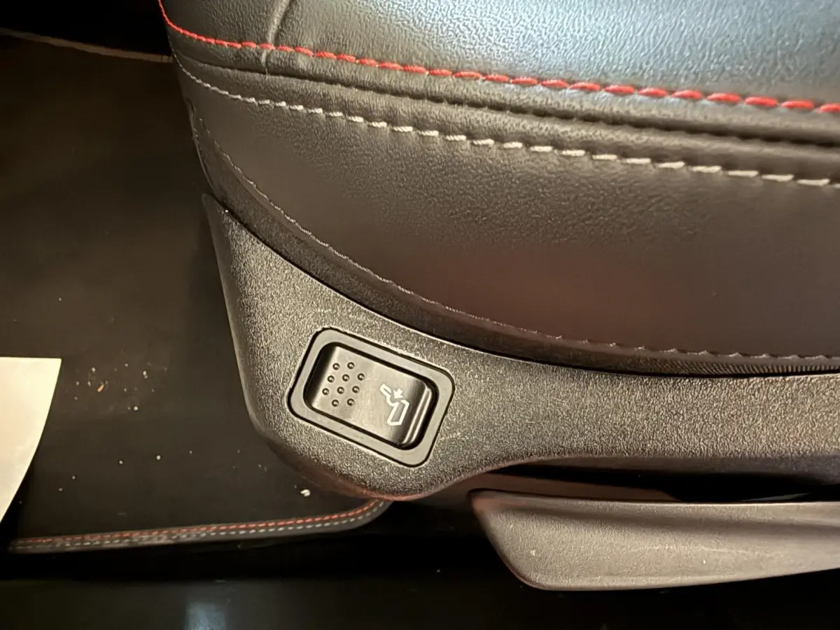 Gros plan sur le bouton de réglage de siège avec surpiqûres rouges sur cuir noir dans une Fiat 500X 2021 Sport.