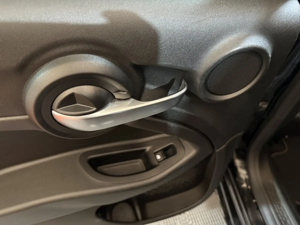 Poignée intérieure de porte côté gauche noire avec haut-parleur rond sur Fiat 500X noir, vue rapprochée depuis l'intérieur.