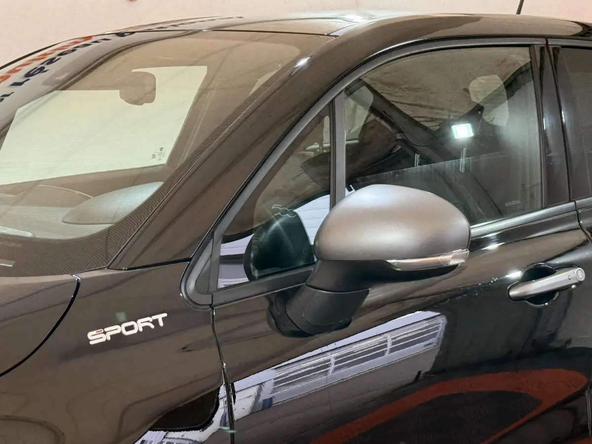 Vue rapprochée du côté gauche d'une FIAT 500X noire avec logo Sport et rétroviseur argenté mat.