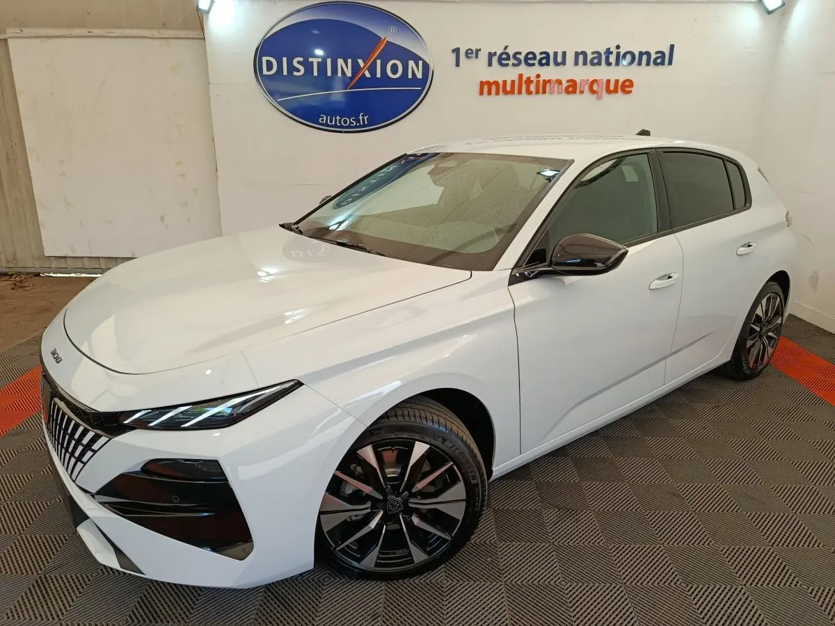 Peugeot 308 blanc vue 3/4 avant droit, avec jantes alliage noires et calandre distinctive en showroom.