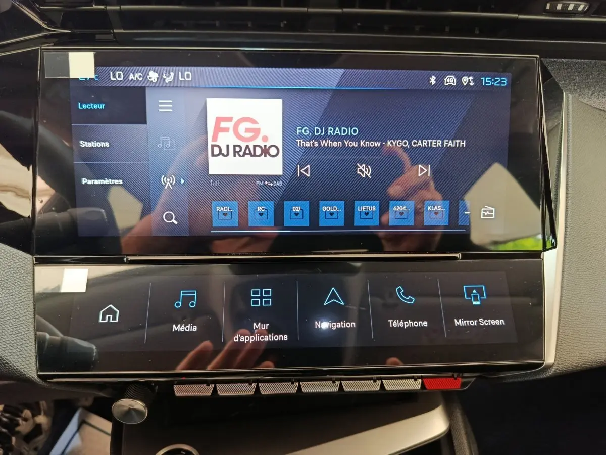 Écran tactile central de la Peugeot 308 blanc, affichant la radio FG DJ Radio avec commandes multimédia.
