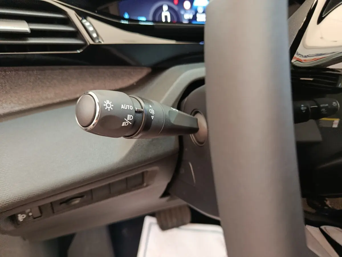 Gros plan sur la commande des feux à gauche du volant cuir dans l’habitacle sombre de la Peugeot 308 blanche 2026.