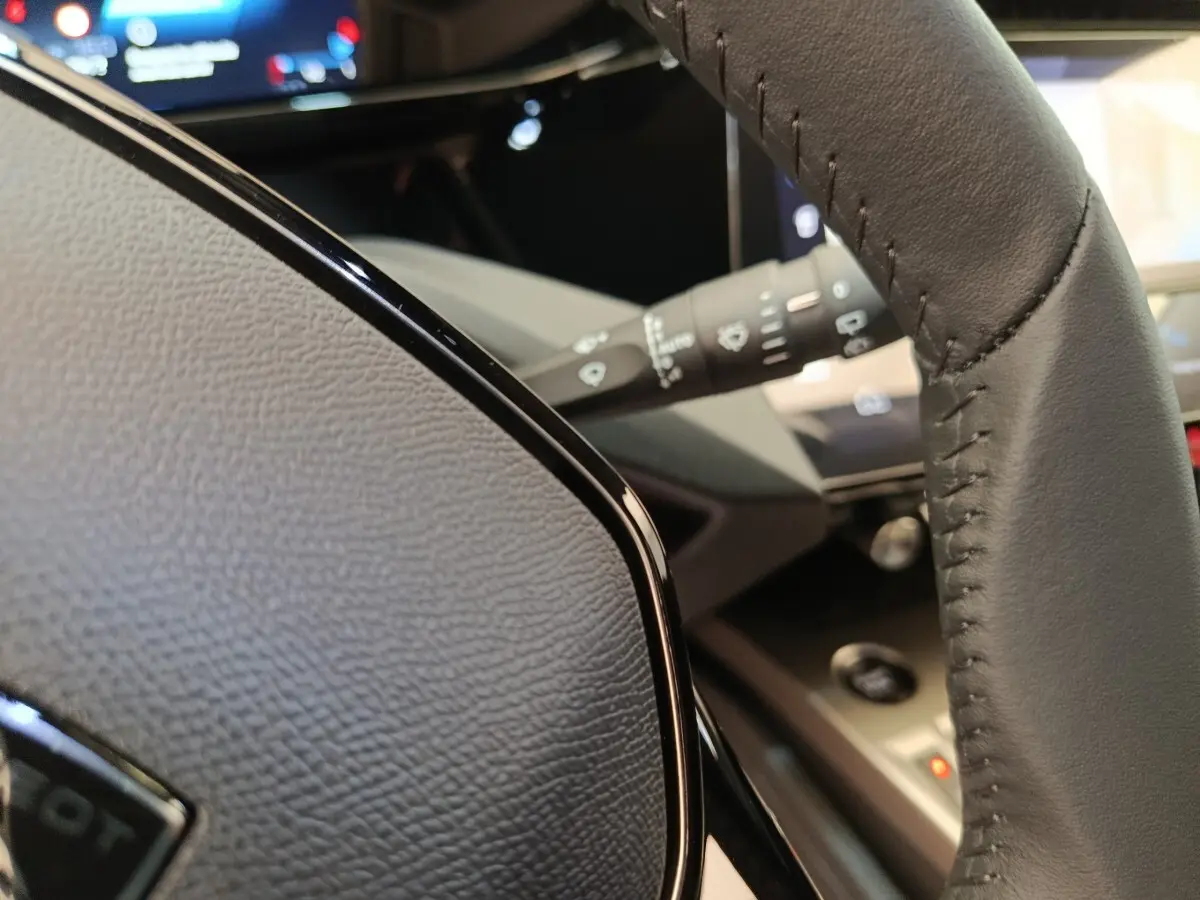 Gros plan sur le volant cuir gris de la Peugeot 308 2026, avec tableau de bord numérique en arrière-plan.