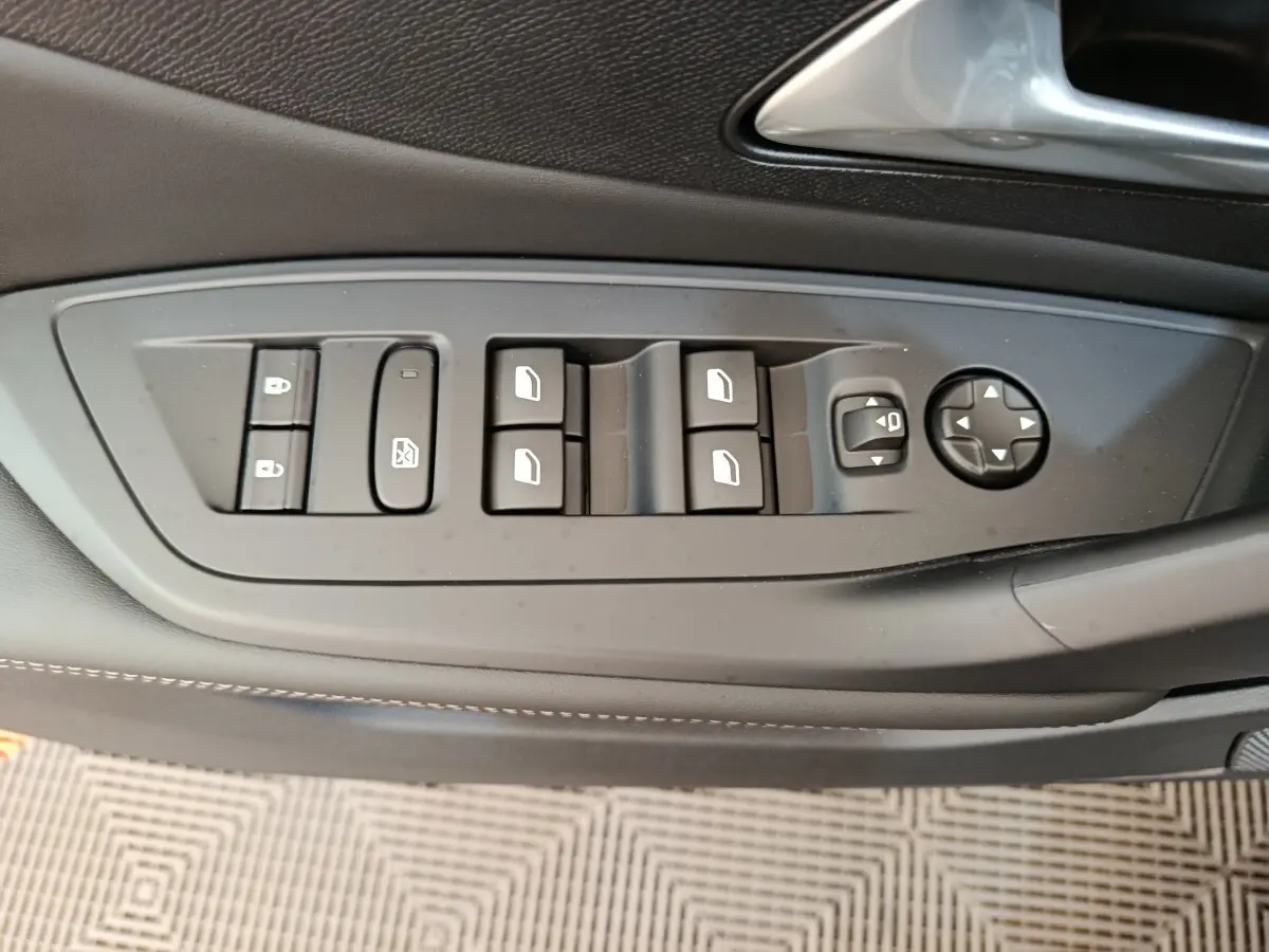 Gros plan sur les commandes de lève-vitres et rétroviseurs côté conducteur de la Peugeot 308 blanche 2026.