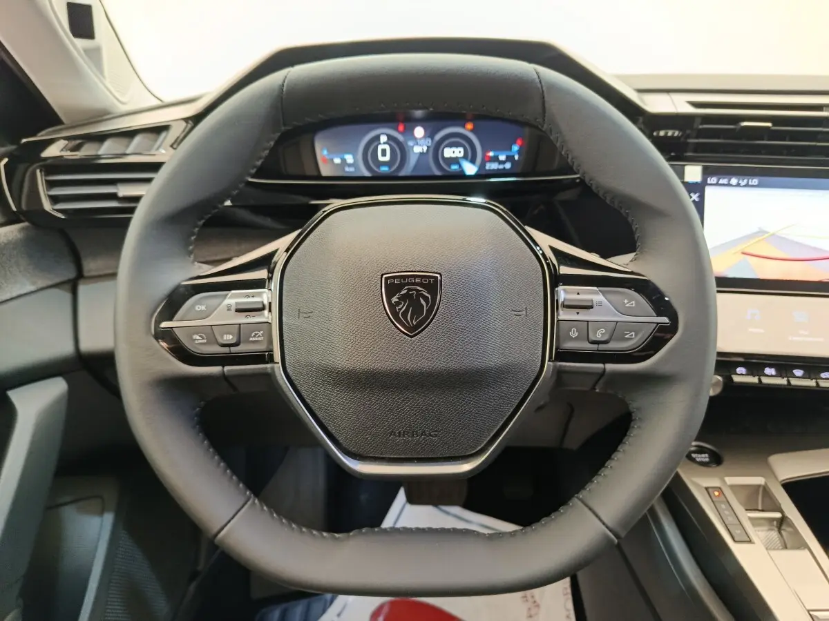 Vue rapprochée du volant cuir noir multifonctions de la Peugeot 308 2026 avec tableau de bord digital et écran tactile.