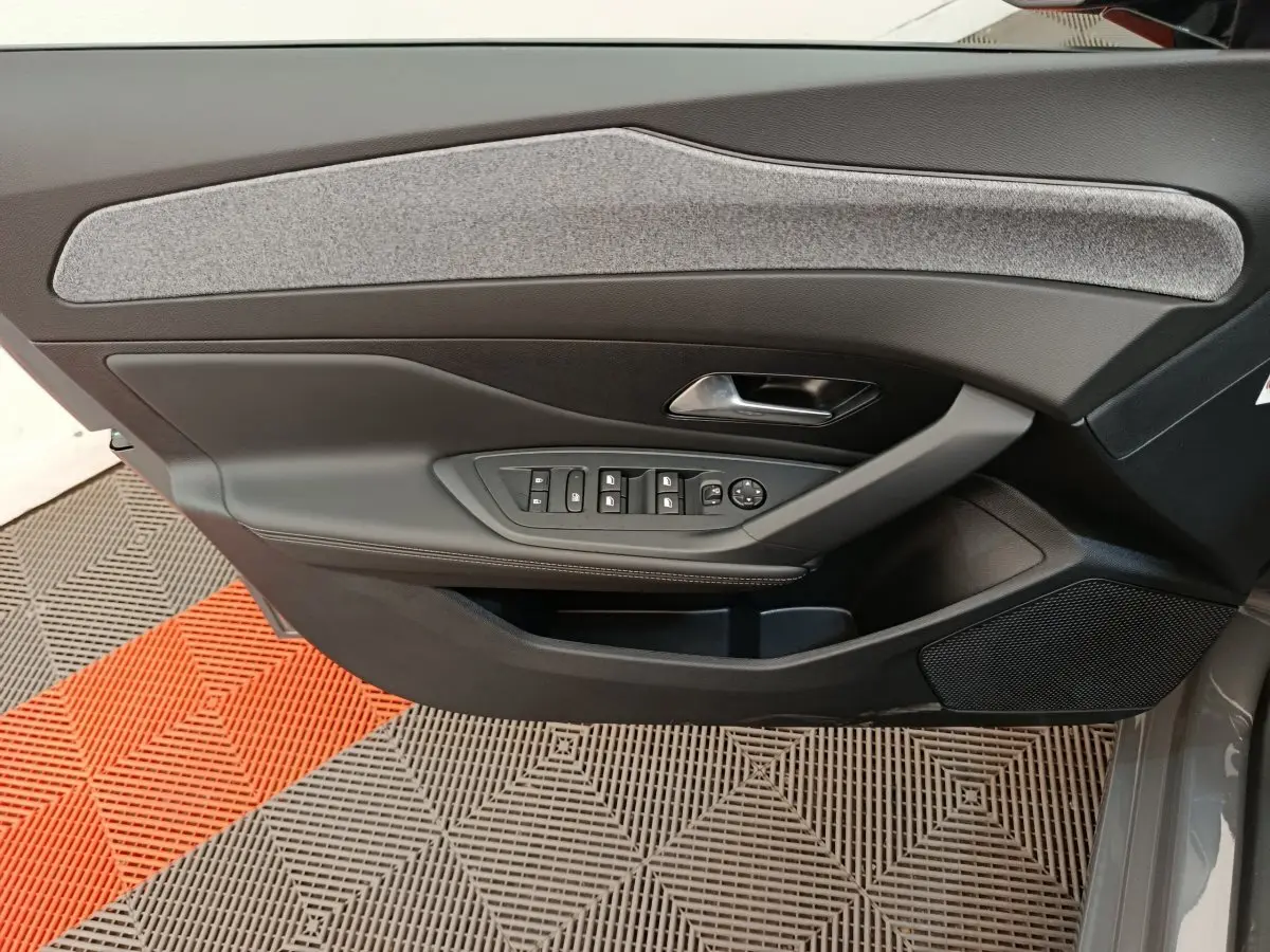 Vue intérieure côté gauche de la porte avant d'une Peugeot 308 blanche, avec commandes électriques et garniture grise.