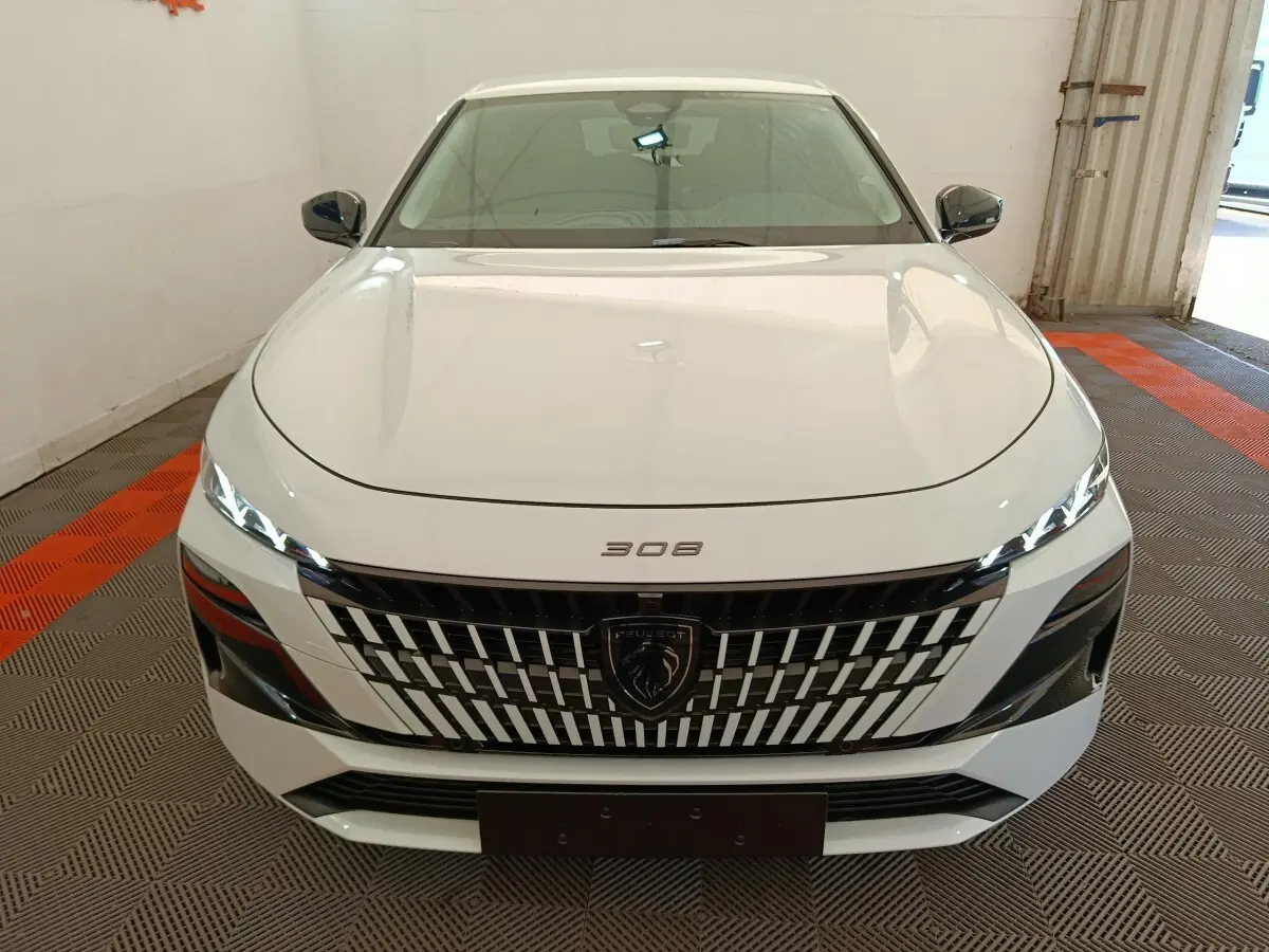 Vue avant d'une Peugeot 308 blanche 2026 avec calandre distinctive et phares LED fins allumés.