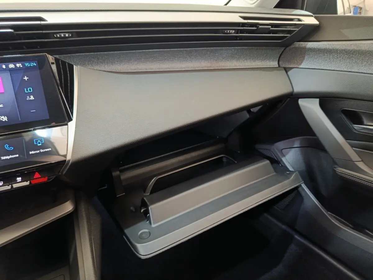 Vue intérieure côté passager de la Peugeot 308 2026 avec boîte à gants ouverte et tableau de bord noir.
