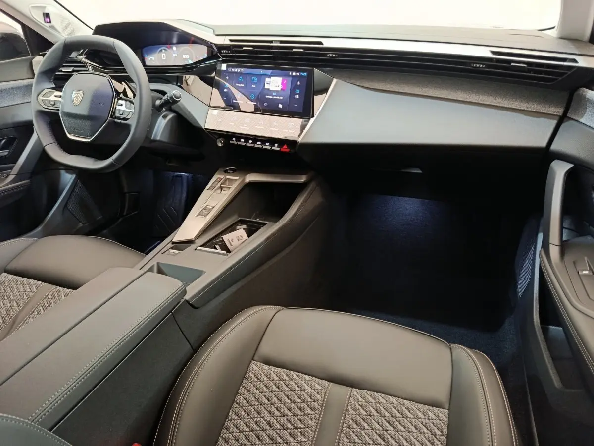 Vue intérieure côté conducteur de la Peugeot 308 2026, volant cuir multifonctions et écran tactile central lumineux.
