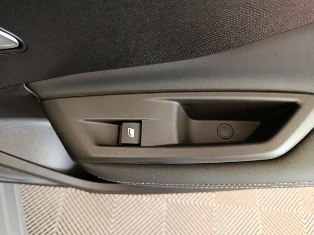 Gros plan sur la poignée intérieure noire de porte côté gauche de la Peugeot 308 blanche, avec bouton de commande de vitre.