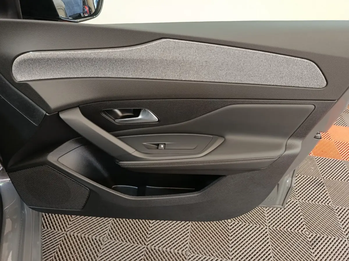 Vue intérieure de la porte côté droit de la Peugeot 308 blanche, avec garniture tissu gris et commandes de fenêtre.