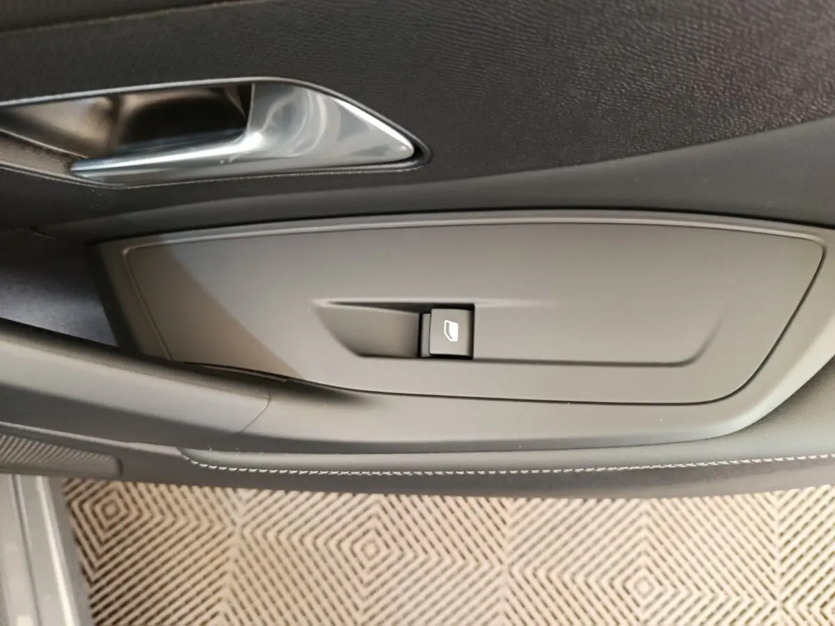 Gros plan sur la commande de lève-vitre côté conducteur de la Peugeot 308 blanche, finition Allure 2026.