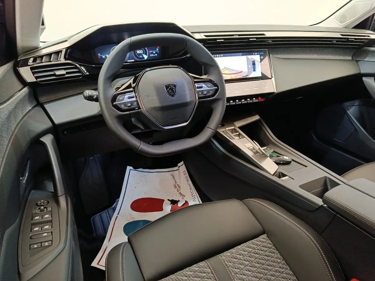 Vue intérieure côté conducteur du tableau de bord et volant cuir noir de la Peugeot 308 blanche 2026.