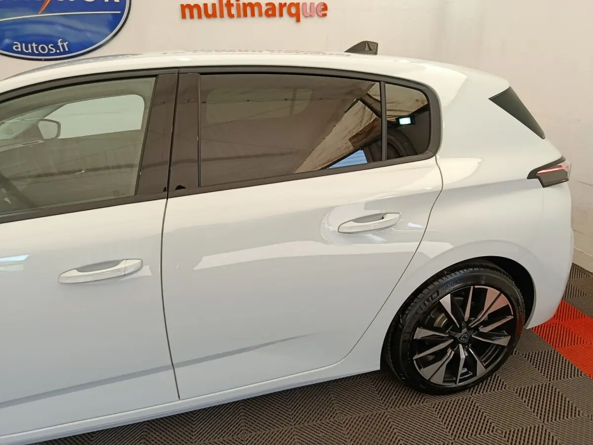 Vue latérale droite d'une Peugeot 308 blanche avec jantes alliage noires et vitres teintées.
