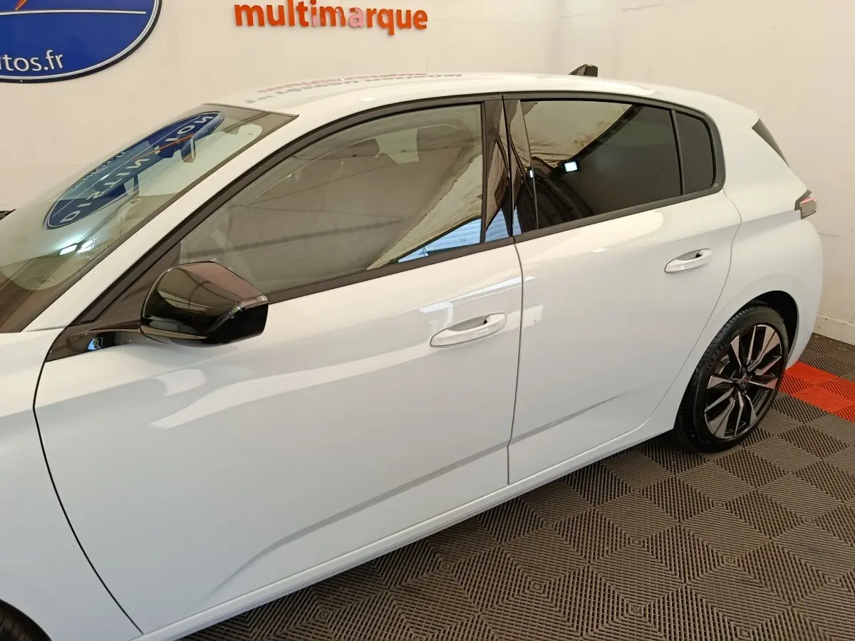 Vue latérale droite d'une Peugeot 308 blanche avec vitres teintées et jantes alliage noires et argentées.