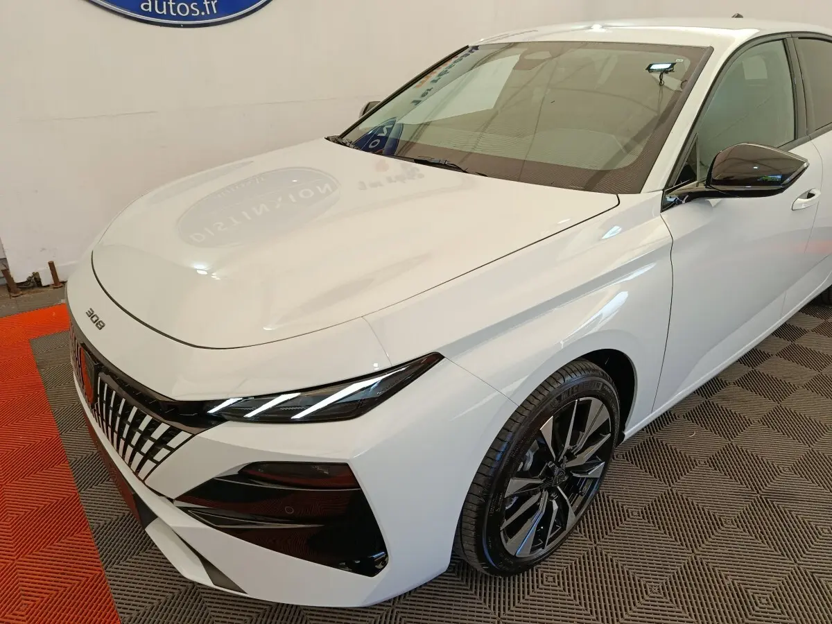 Peugeot 308 blanc vue 3/4 avant droit, avec calandre distinctive et jantes alliage noires brillantes.