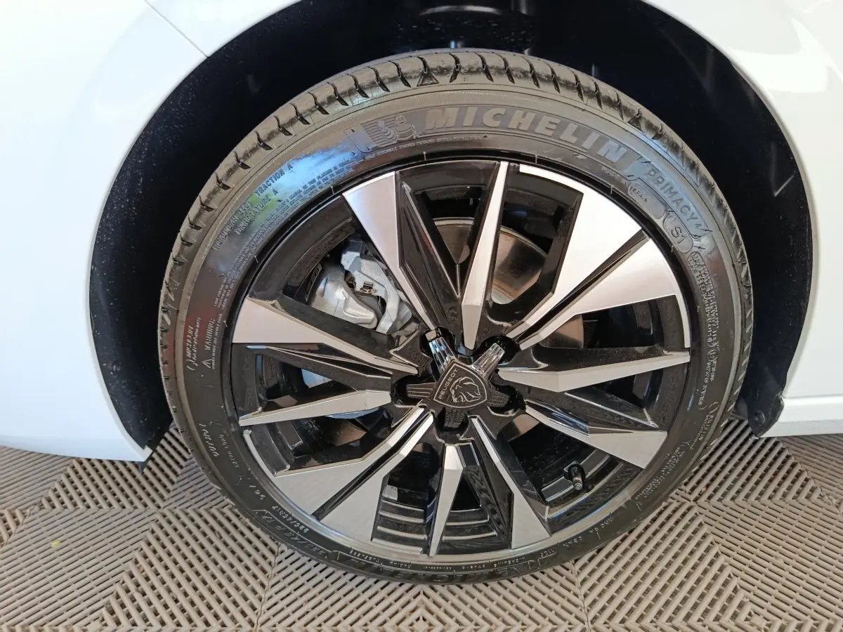 Gros plan sur la roue avant droite d'une Peugeot 308 blanche, jante alliage noire et argentée au design moderne.
