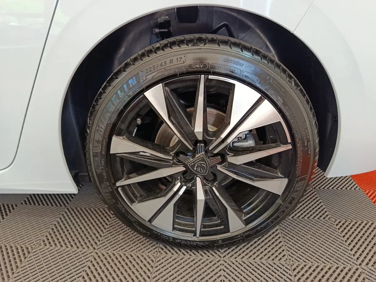 Gros plan sur la roue avant droite d’une Peugeot 308 blanche avec jante alliage noire et argentée au design moderne.
