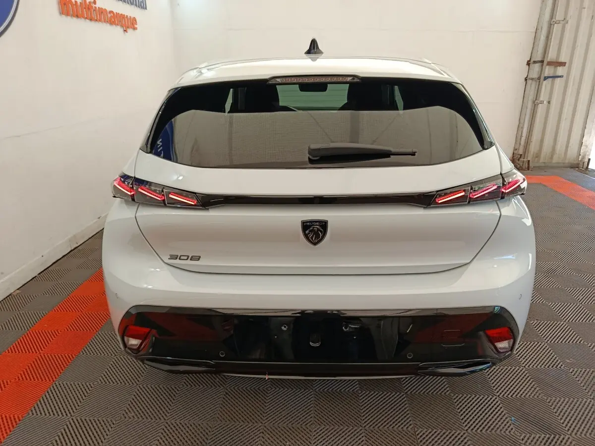 Vue arrière d'une Peugeot 308 blanche 2026 avec feux LED distinctifs et logo noir au centre du hayon.