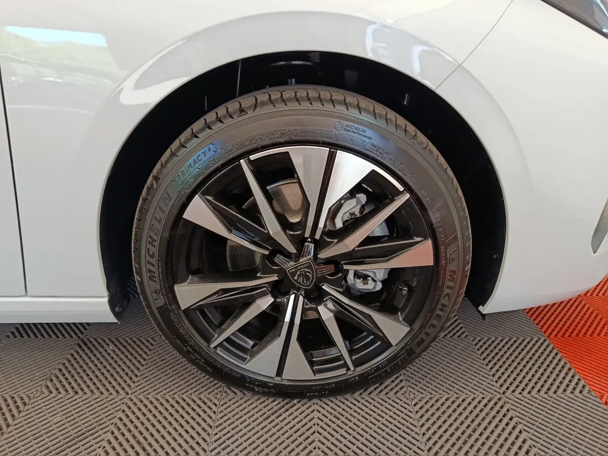 Gros plan sur la roue avant gauche de la Peugeot 308 blanche, avec jante alliage noire et argentée au design moderne.