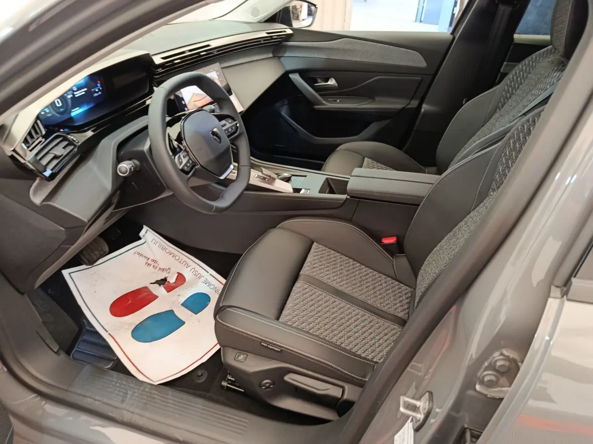 Vue intérieure côté conducteur de la Peugeot 308 blanche 2026, volant cuir multifonctions et sièges tissu-cuir gris.