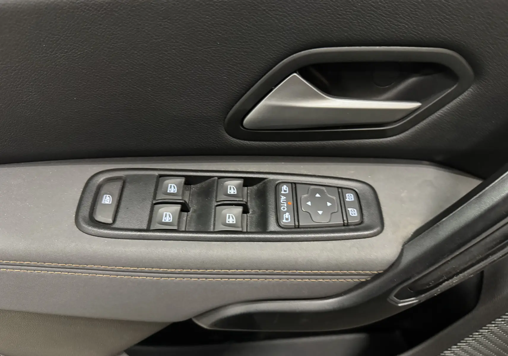 Gros plan sur la commande des vitres électriques et la poignée intérieure côté gauche du Dacia Duster 2024, finition tissu gris.