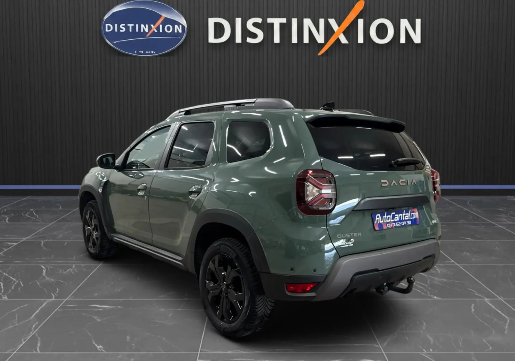 Vue 3/4 arrière droite du Dacia Duster 2024 kaki lichen avec jantes noires et barres de toit, dans un showroom intérieur.