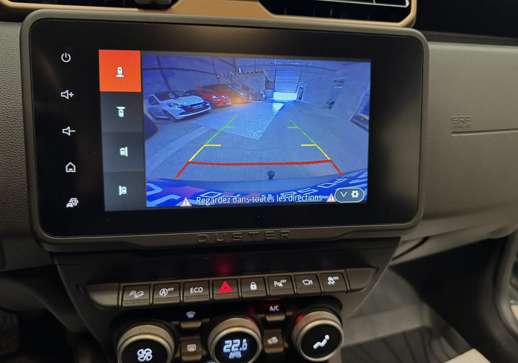 Écran tactile intérieur du Dacia Duster 2024 montrant la caméra de recul avec vue arrière sur un parking.