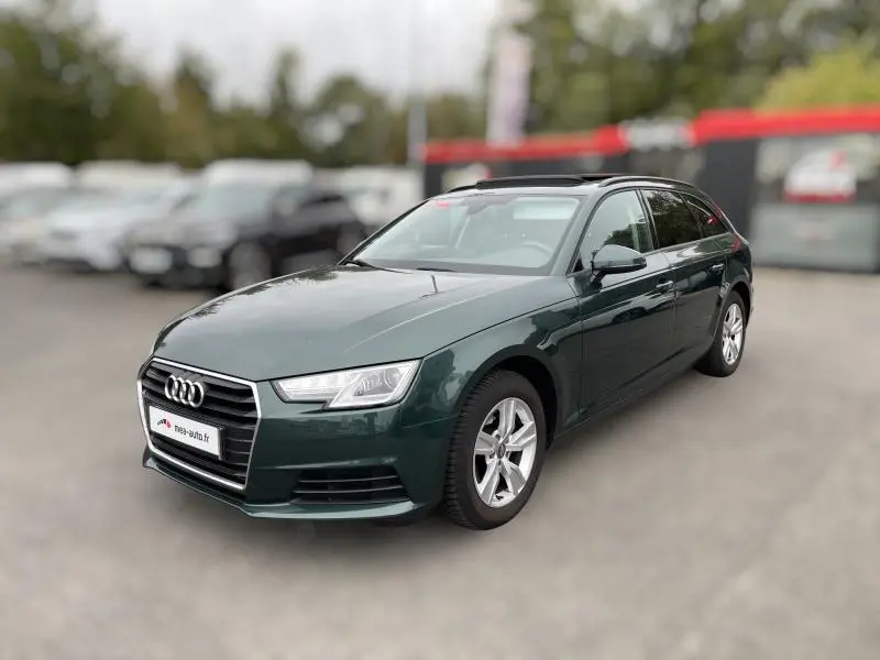 Audi A4 Avant vert foncé vue 3/4 avant droit avec jantes alu et vitres surteintées sur parking flou.