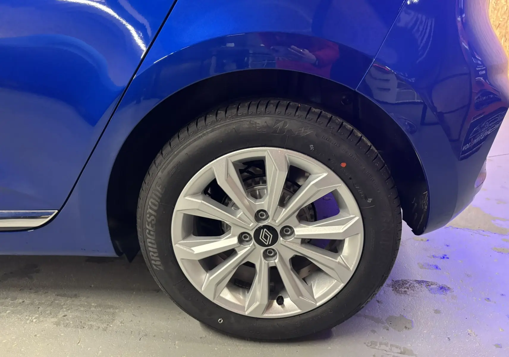 Gros plan sur la roue arrière droite de la Renault Clio 2024 bleu iron avec jante alliage argentée au design moderne.