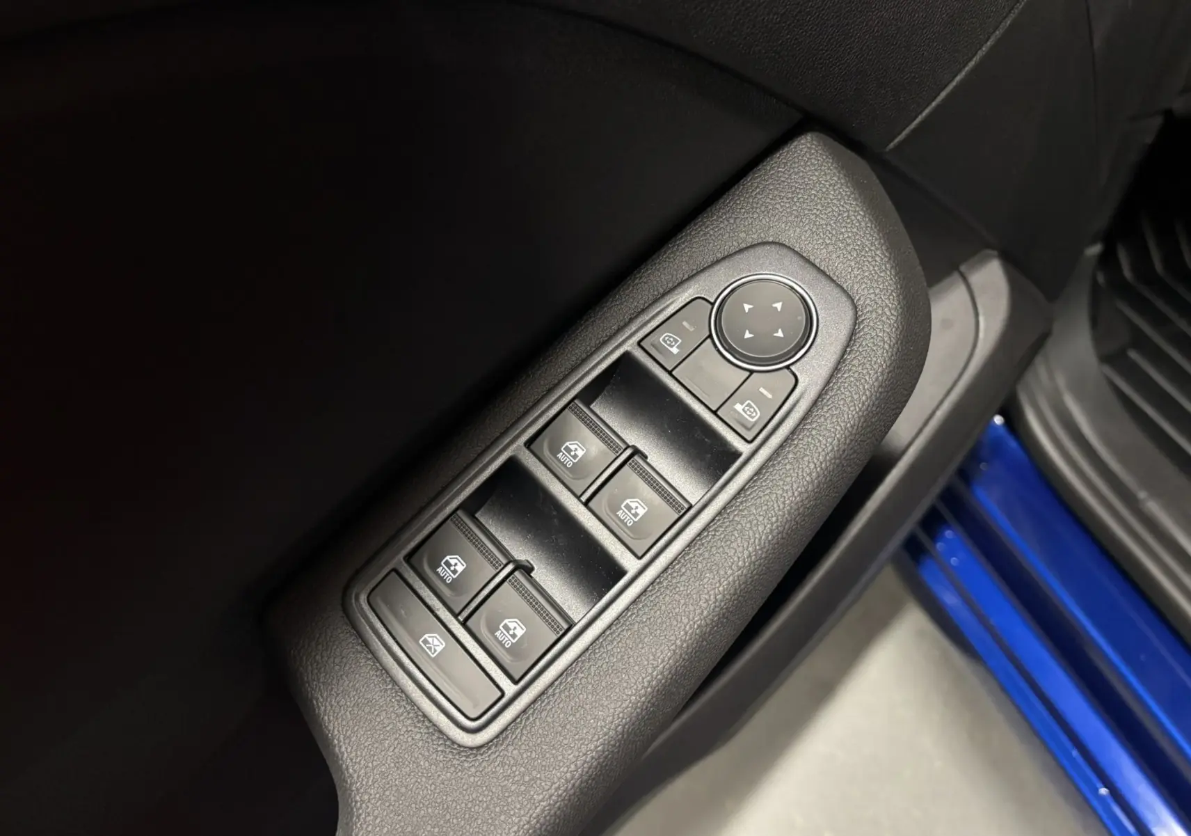 Gros plan sur les commandes des vitres électriques côté gauche, avec partie de la porte bleu iron visible en bas à droite.