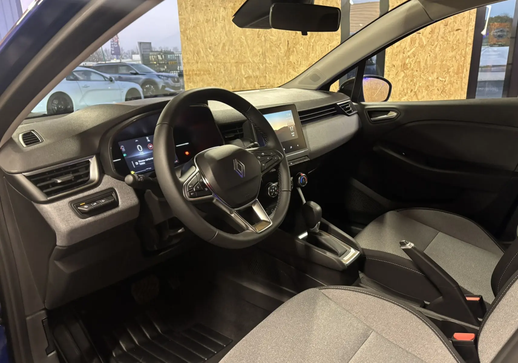 Vue intérieure côté conducteur de la Renault Clio 2024, avec volant multifonction et sellerie tissu gris noir.