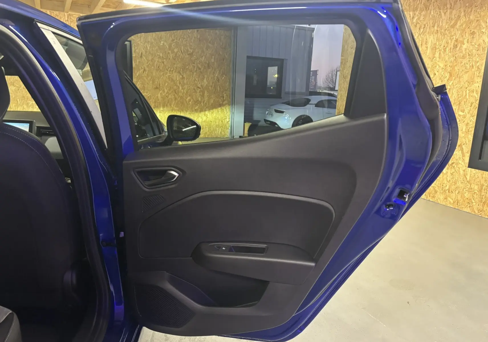 Vue intérieure de la porte arrière droite bleu iron d’une Renault Clio 2024, montrant la garniture noire et la poignée intégrée.