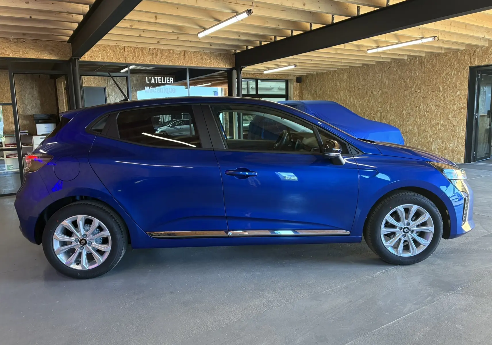 Profil droit d'une Renault Clio TCE 90ch X-Tronic Evolution 2024 en bleu Iron, avec jantes alliage et intérieur gris-noir visible.