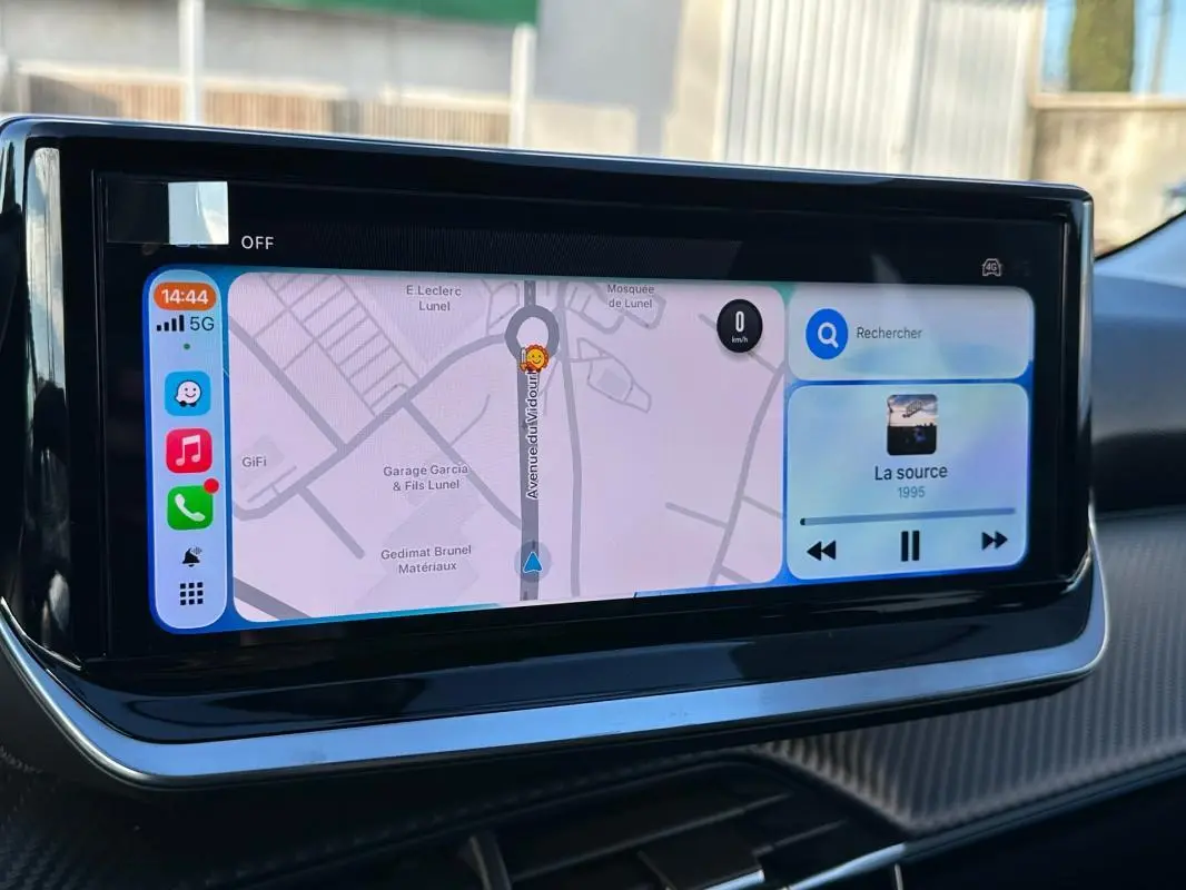 Écran tactile du tableau de bord de la Peugeot 208 Hybrid blanc, affichant navigation et musique en cours.