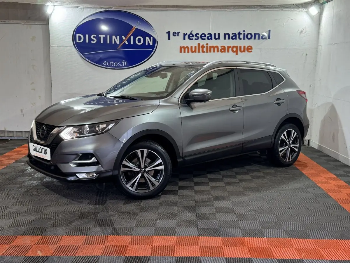 Nissan Qashqai gris foncé en 3/4 avant droit, avec jantes alliage et feux LED, dans un showroom intérieur.