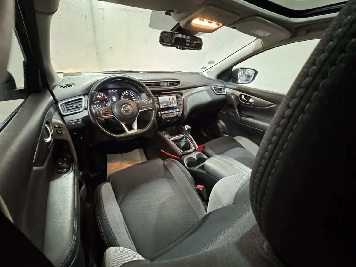 Vue intérieure avant du Nissan Qashqai 2019 gris foncé, volant cuir alu multifonctions et écran tactile central visible.