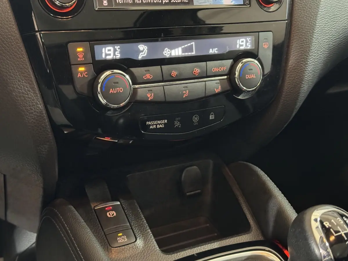 Gros plan sur la console centrale du Nissan Qashqai gris foncé, montrant la climatisation digitale et le frein à main électrique.