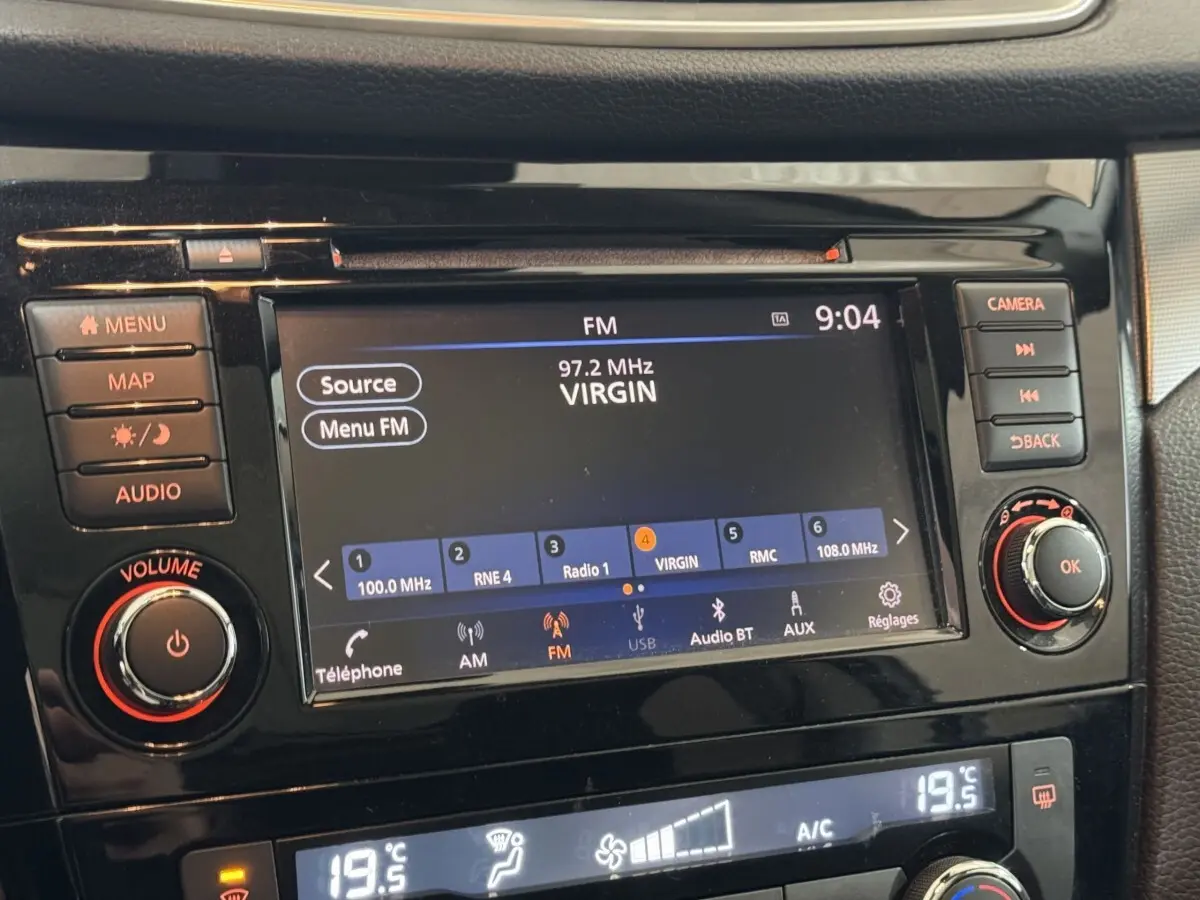 Gros plan sur l’écran tactile central noir du Nissan Qashqai gris foncé, affichant la radio FM et commandes audio.