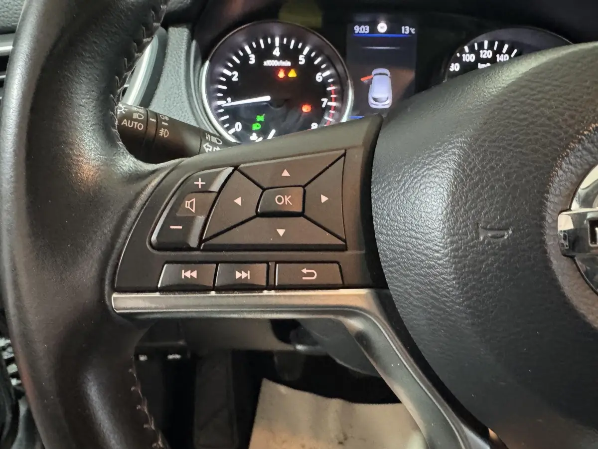 Gros plan sur le volant cuir et alu côté gauche du Nissan Qashqai gris foncé, avec commandes multifonctions et tableau de bord lumineux.