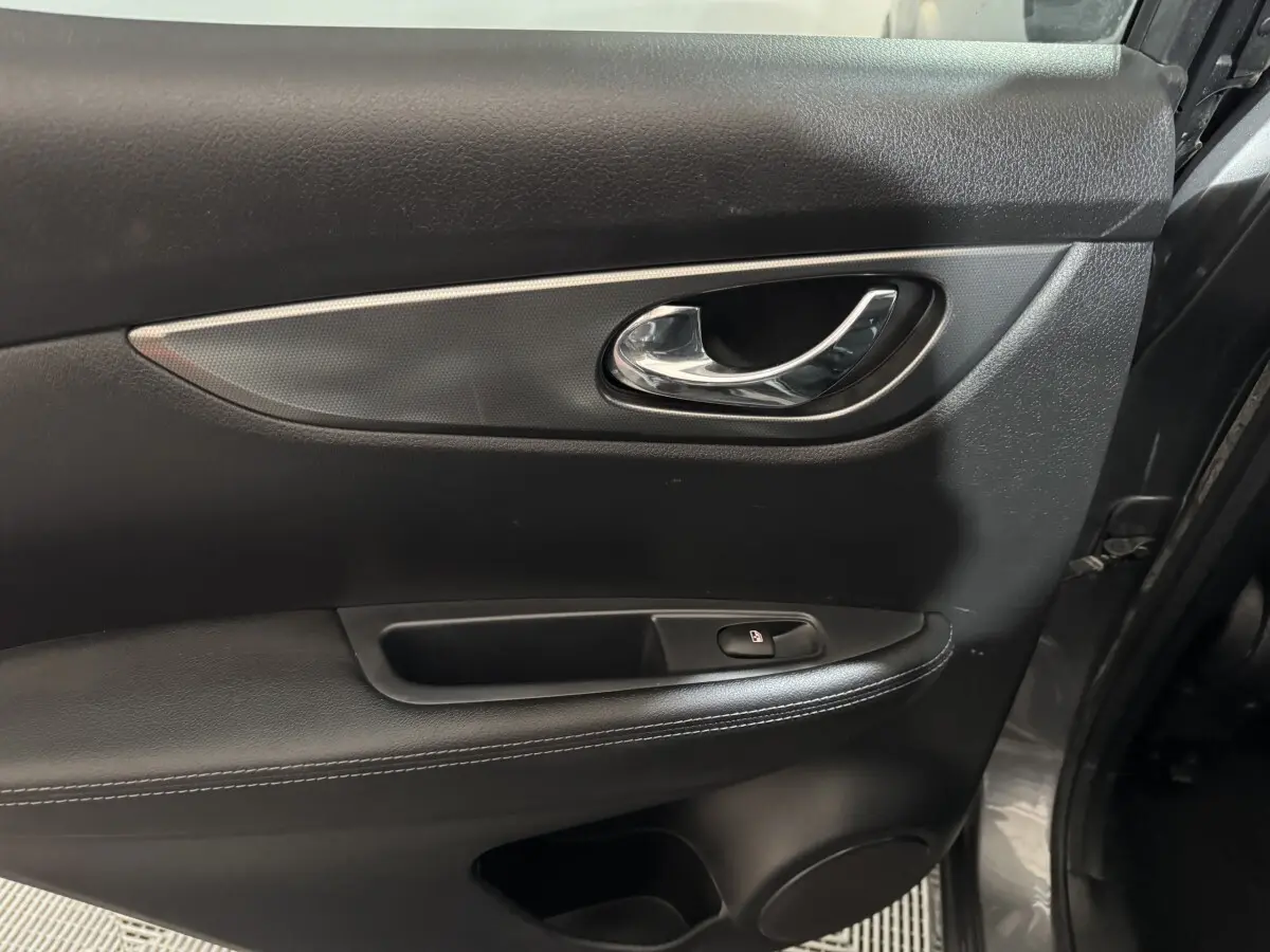 Gros plan sur la porte intérieure côté gauche du Nissan Qashqai gris foncé, avec poignée chrome et bouton de verrouillage.