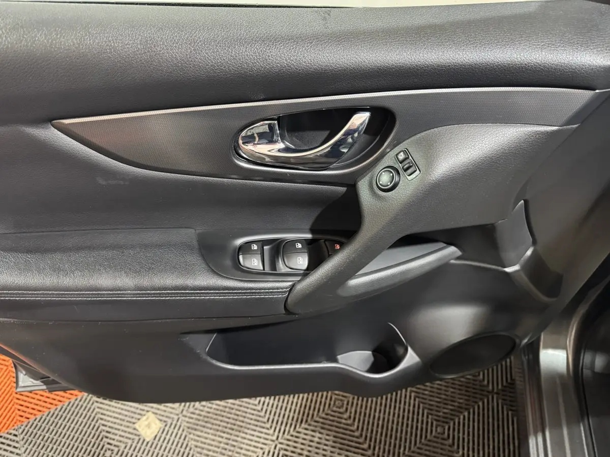 Gros plan sur la porte intérieure côté conducteur du Nissan Qashqai gris foncé, avec commandes de vitres et poignée chromée.