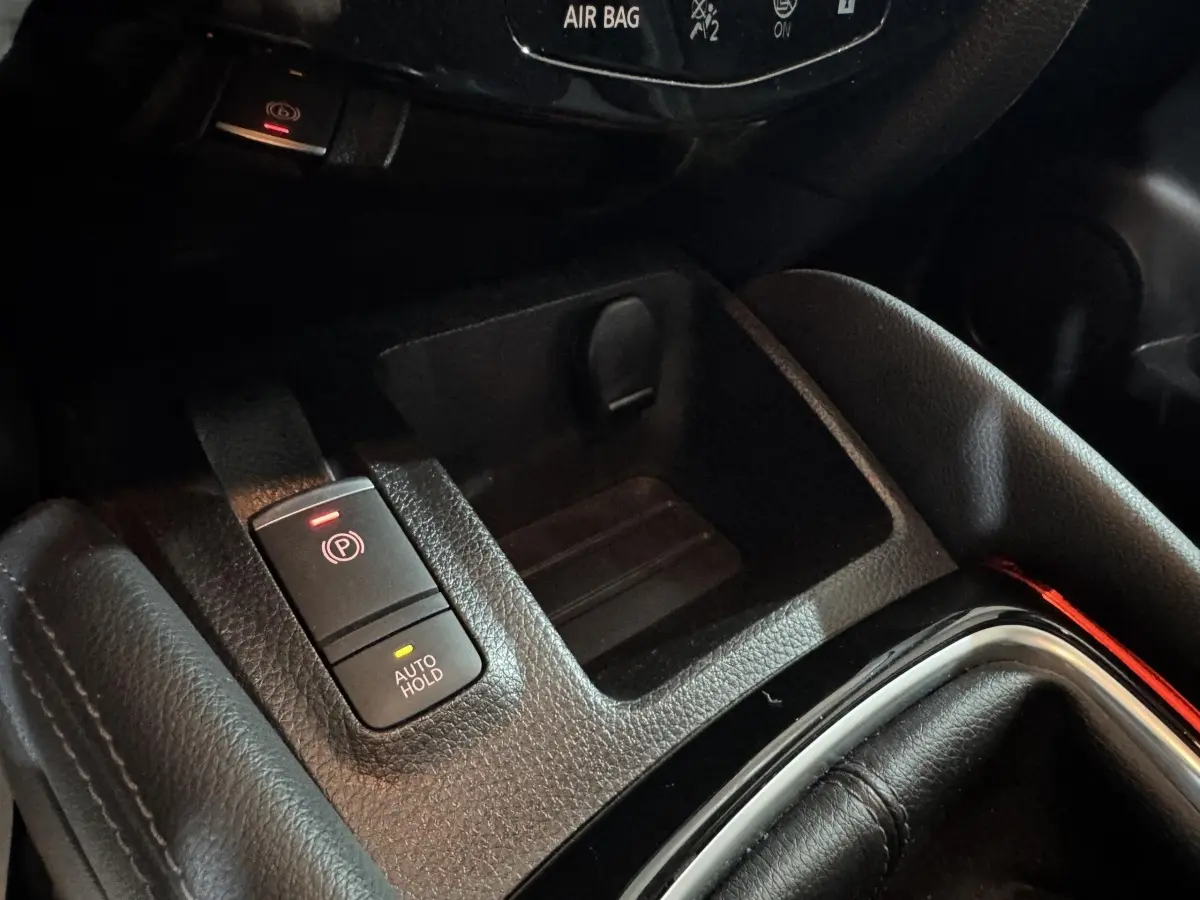 Gros plan sur la console centrale du Nissan Qashqai gris foncé, montrant le frein à main électrique et le bouton Auto Hold.